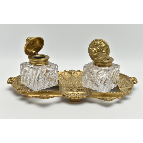 395A - A LATE VICTORIAN BRASS INKSTAND FITTED WITH TWO SQUARE MOULDED GLASS INKWELLS, the stand cast with s... 