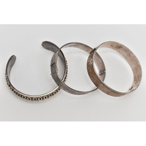 89 - TWO SILVER HINGED BANGLES AND A WHITE METAL CUFF BRACELET, the first a flat hinged bangle with folia... 