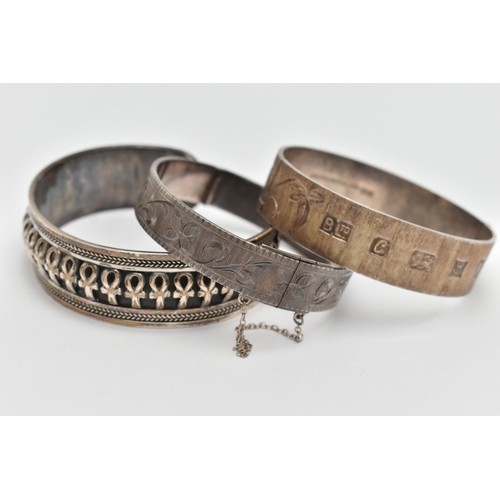 89 - TWO SILVER HINGED BANGLES AND A WHITE METAL CUFF BRACELET, the first a flat hinged bangle with folia... 