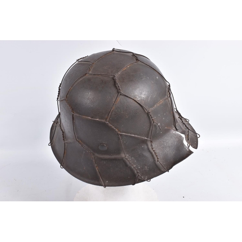 469 - A BATTLE DAMAGED WWII ERA GERMAN STEEL HELMET WITH CAMOUFLAGE WIRE NETTING,  this helmet still has a... 