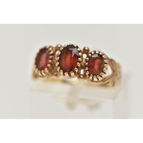 18 - A 9CT GOLD GARNET RING, designed as three graduated oval garnets in claw settings to the scrolling s... 