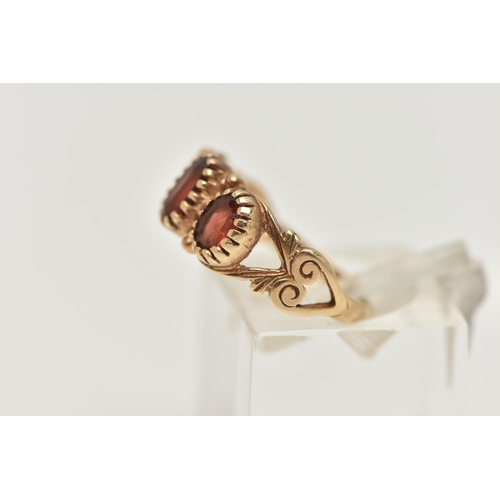 18 - A 9CT GOLD GARNET RING, designed as three graduated oval garnets in claw settings to the scrolling s... 