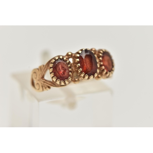 18 - A 9CT GOLD GARNET RING, designed as three graduated oval garnets in claw settings to the scrolling s... 