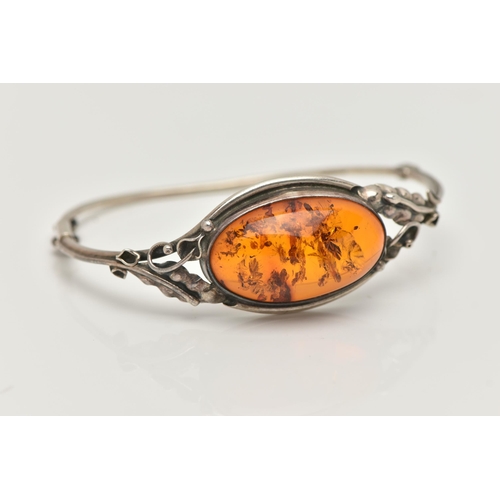 19 - A SILVER AMBER BANGLE, designed as an oval cabochon of heated amber within a collet mount to the bif... 