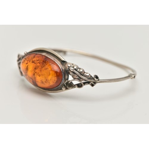 19 - A SILVER AMBER BANGLE, designed as an oval cabochon of heated amber within a collet mount to the bif... 