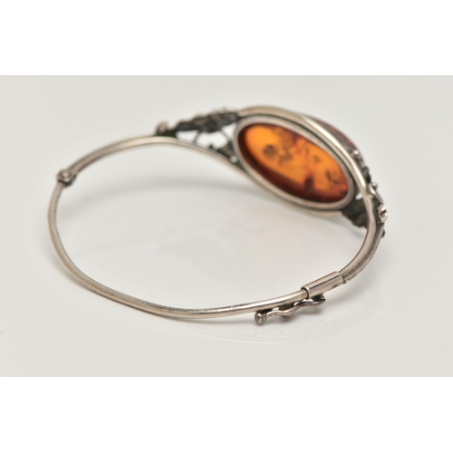 19 - A SILVER AMBER BANGLE, designed as an oval cabochon of heated amber within a collet mount to the bif... 