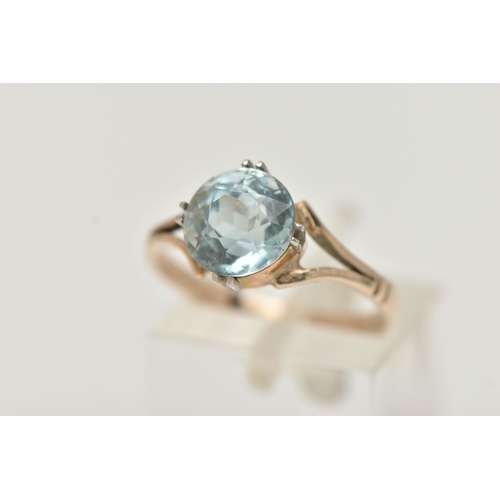 23 - AN AQUAMARINE RING, designed as a circular cut aquamarine in a double four claw setting to the bifur... 