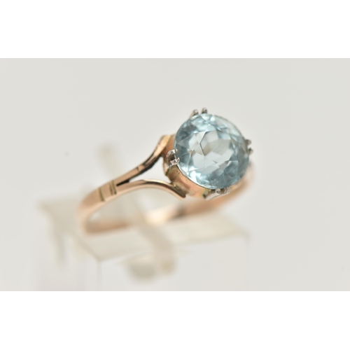 23 - AN AQUAMARINE RING, designed as a circular cut aquamarine in a double four claw setting to the bifur... 