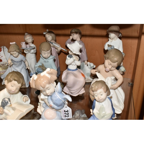 372 - ELEVEN NAO FIGURES OF CHILDREN, to include a boy reading to a puppy, a girl with a toy rabbit, a gir... 