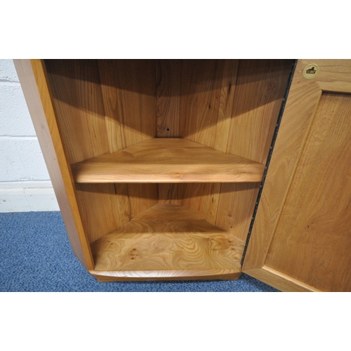 1249 - AN ERCOL ELM CORNER CUPBOARD, with two shelves, above a single cupboard door enclosing another shelf... 