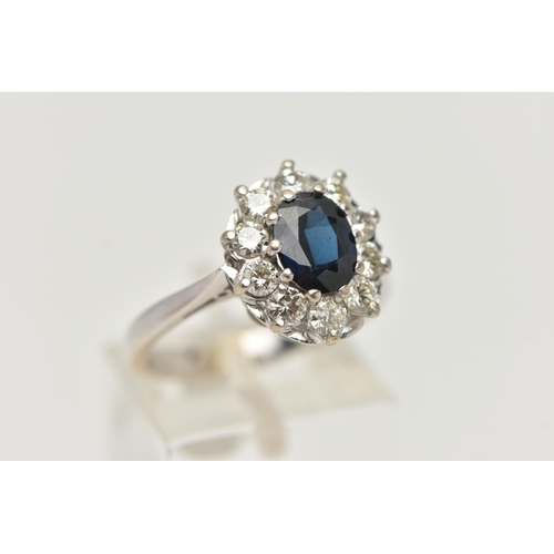 13 - AN 18CT WHITE GOLD SAPPHIRE AND DIAMOND CLUSTER RING, the oval sapphire within a ten claw setting su... 