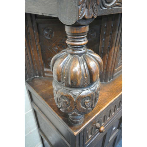 1256 - A 20TH CENTURY OAK COURT CUPBOARD, the top with a single cupboard door, scrolled and foliate carved ... 