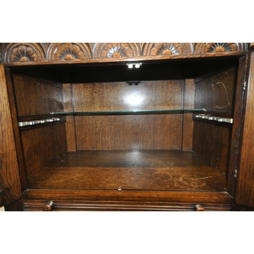 1211 - A 20TH CENTURY SOLID OAK DRINKS CABINET, the two double doors , carved with a seated person, an arch... 