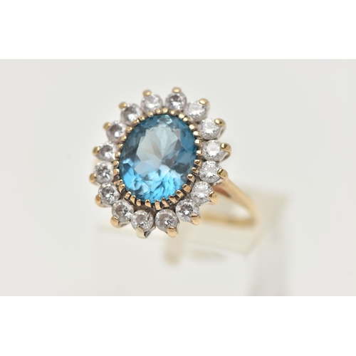 144 - A 9CT GOLD CLUSTER RING, centring on an oval cut blue topaz, in a surround of colourless cubic zirco... 