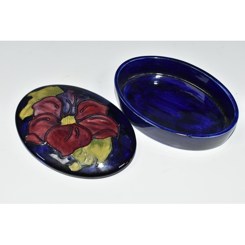 358 - A MOORCROFT POTTERY CLEMATIS TRINKET BOX, the oval box in purple Clematis pattern on a cobalt blue g... 