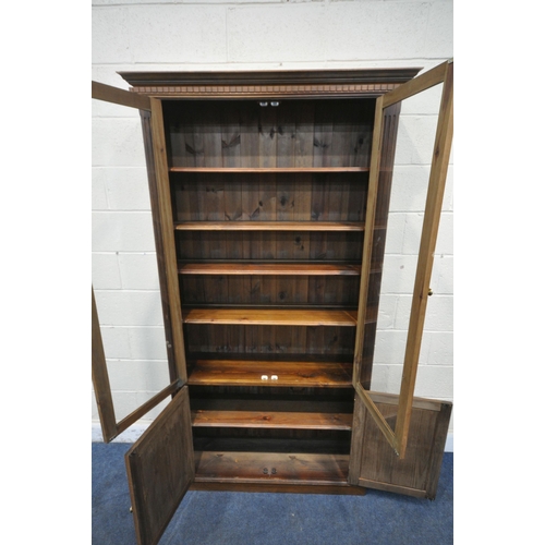 1253 - A LARGE PINE BOOKCASE, the two glazed doors enclosing four adjustable shelves, above two cupboard do... 