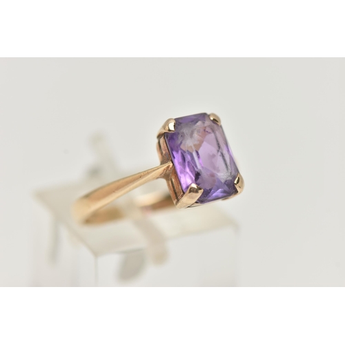 25 - A YELLOW METAL GEM SET RING, rectangular cut purple stone assessed as amethyst, prong set in yellow ... 