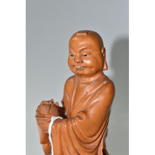 364 - AN ORIENTAL CARVED WOOD FIGURINE, a boxwood carved figure of a smiling Chinese monk bearing a basket... 