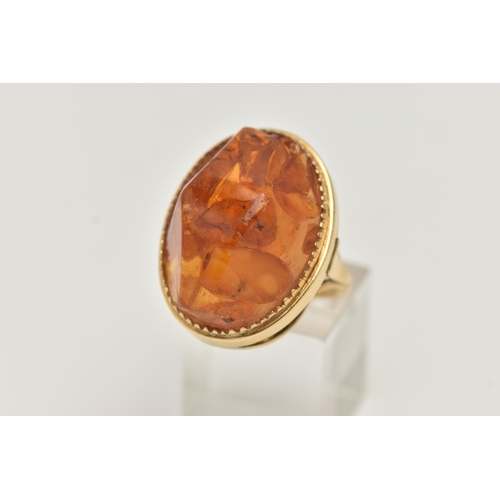 27 - A PRESSED AMBER RING, designed as a large oval piece of pressed amber within a collet style setting,... 