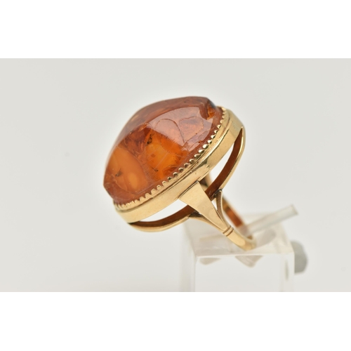 27 - A PRESSED AMBER RING, designed as a large oval piece of pressed amber within a collet style setting,... 