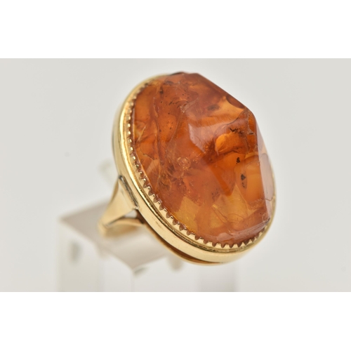 27 - A PRESSED AMBER RING, designed as a large oval piece of pressed amber within a collet style setting,... 