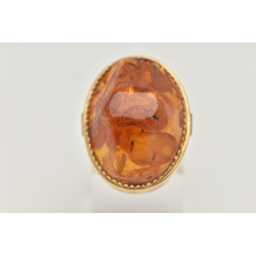 27 - A PRESSED AMBER RING, designed as a large oval piece of pressed amber within a collet style setting,... 