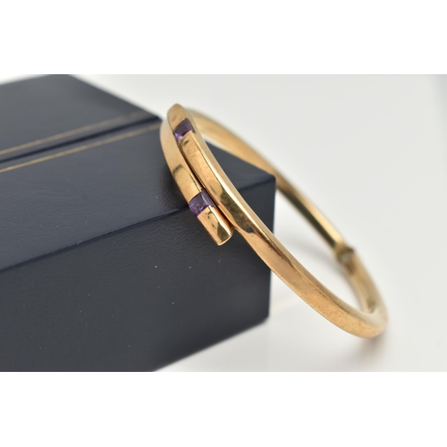 67 - A 9CT GOLD AMETHYST BANGLE, the crossover bangle with sprung hinge, set to each terminal with a squa... 