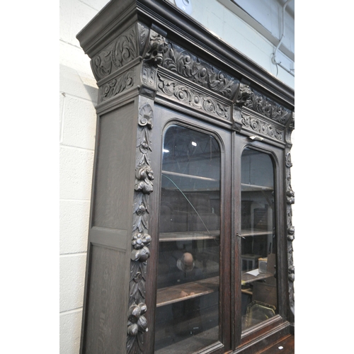 1198 - A LATE 19TH / EARLY 20TH CENTURY CARVED OAK GLAZED BOOKCASE, depicting lions masks and other detail,... 