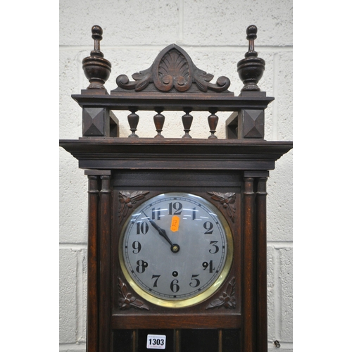 1303 - AN EARLY 20TH CENTURY WALL CLOCK, with finals and spindles above a full length door enclosing a silv... 