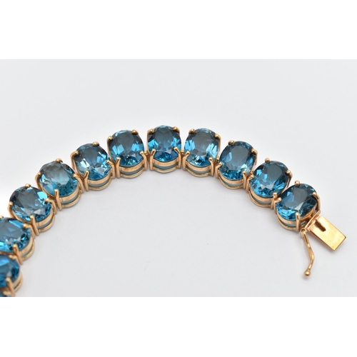 33 - A 9CT YELLOW GOLD TOPAZ BRACELET, designed as a series of approximately twenty-three oval blue topaz... 