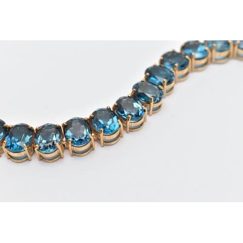 33 - A 9CT YELLOW GOLD TOPAZ BRACELET, designed as a series of approximately twenty-three oval blue topaz... 