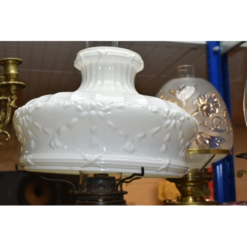 432 - THREE OIL LAMPS AND SHADES, comprising a lamp with a pierced cast iron base and cranberry glass oil ... 