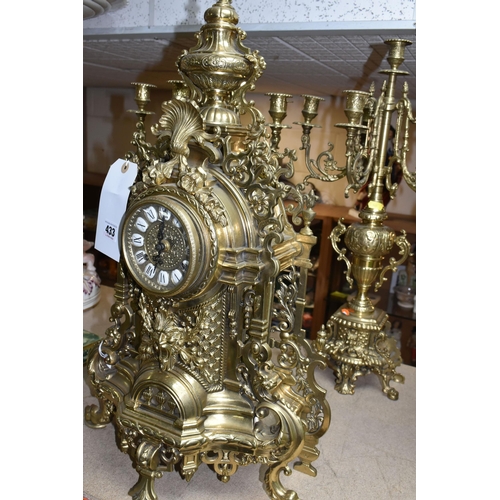 433 - A BRASS FRANZ HERMLE CLOCK GARNITURE, the clock having a chapter ring inset with enamel Roman Numera... 
