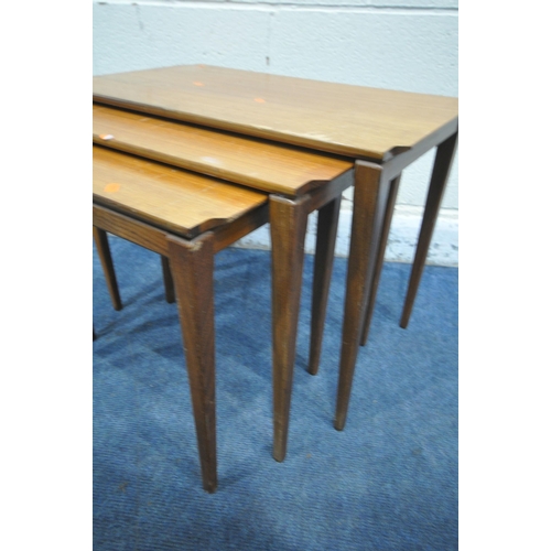 1254 - A MID CENTURY TEAK NEST OF THREE TABLES, with shaped corners, raised on square tapered legs, largest... 