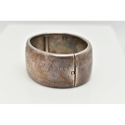 154 - A WHITE METAL HINGED BANGLE, wide bangle engraved with an oriental design, fitted with a push button... 