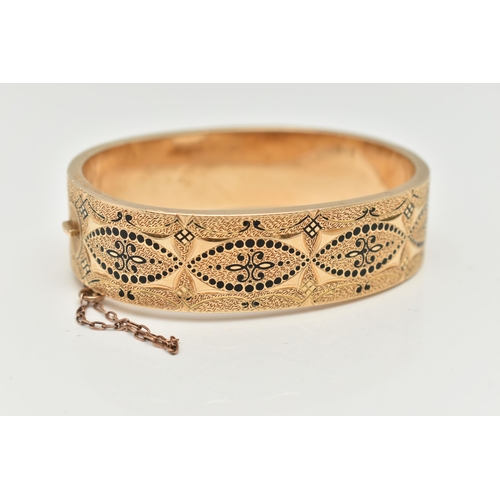 129 - A YELLOW METAL HINGED BANGLE, wide bangle decorated with a black enamel pattern with textured surrou... 