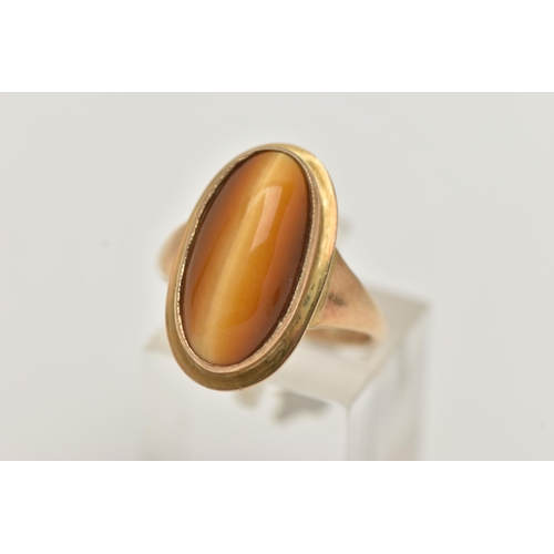 134 - A 9CT GOLD DRESS RING, an elongated oval cabochon tigers eye, collet set in yellow gold, leading on ... 