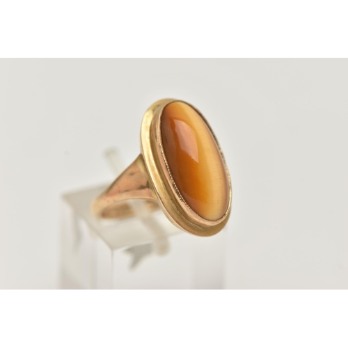 134 - A 9CT GOLD DRESS RING, an elongated oval cabochon tigers eye, collet set in yellow gold, leading on ... 