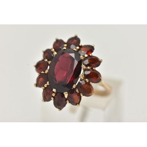 17 - A GARNET CLUSTER RING, designed as a central oval garnet within an oval garnet surround, in claw set... 
