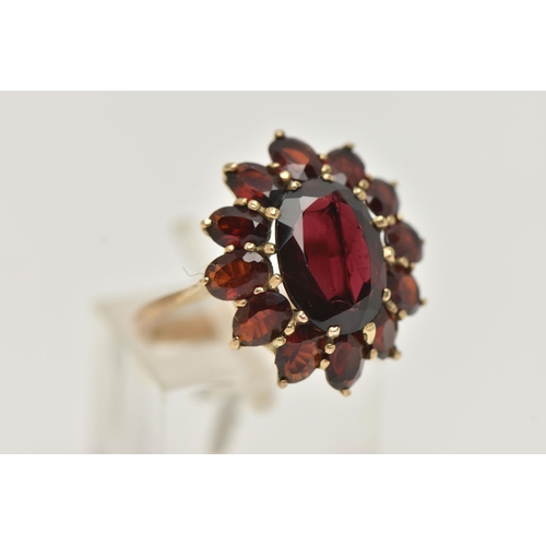 17 - A GARNET CLUSTER RING, designed as a central oval garnet within an oval garnet surround, in claw set... 