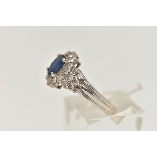 6 - AN 18CT WHITE GOLD SAPPHIRE AND DIAMOND CLUSTER RING, centrally set with an oval cut blue sapphire, ... 