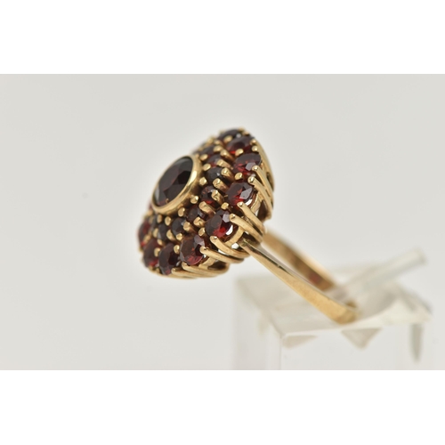 70 - A GARNET CLUSTER RING, the central circular cut garnet in a collet setting within a two tier claw se... 