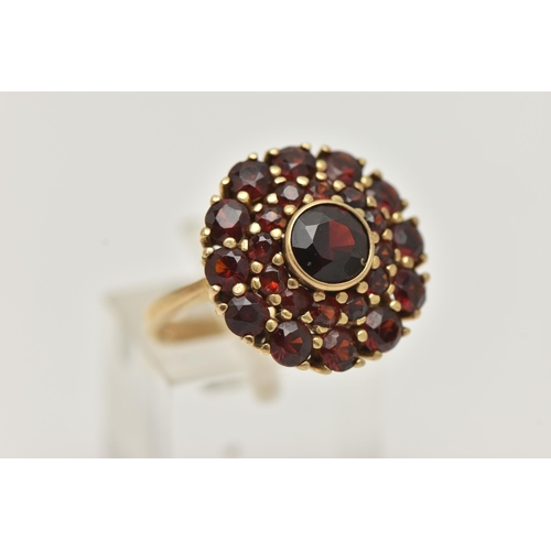 70 - A GARNET CLUSTER RING, the central circular cut garnet in a collet setting within a two tier claw se... 