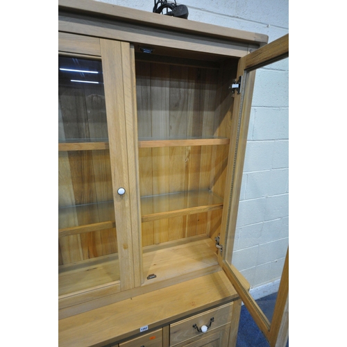 1262 - A MODERN LIGHT OAK BOOKCASE, the double glazed doors enclosing two glass shelves, atop a base fitted... 