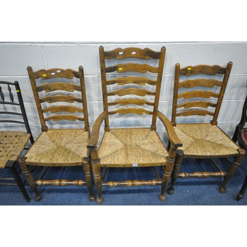 1297 - A SET OF THREE EARLY 20TH CENTURY OAK RUSH SEATED LADDER BACK CHAIRS, including one carver, another ... 