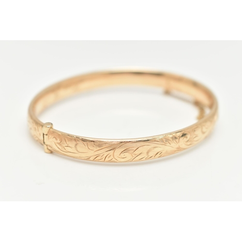 10 - A 9CT GOLD HINGED BANGLE, with engraved scrolling acanthus decoration throughout to the hidden push ... 