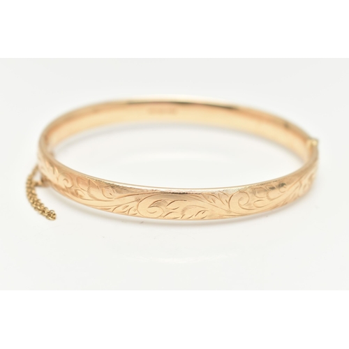 10 - A 9CT GOLD HINGED BANGLE, with engraved scrolling acanthus decoration throughout to the hidden push ... 