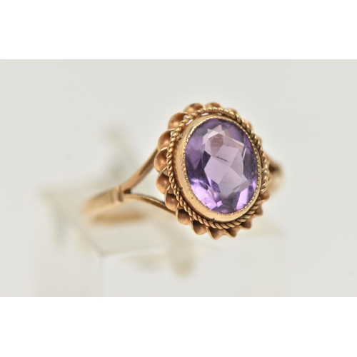 21 - A 9CT GOLD AMETHYST RING, centering on an oval cut amethyst, collet set with a fine rope twist surro... 