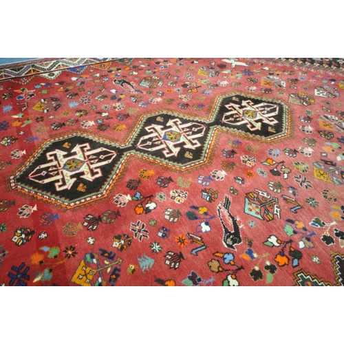 1299 - A WOOLLEN RED GROUND RUG, with a repeating pattern of birds, three central medallions, black filled ... 