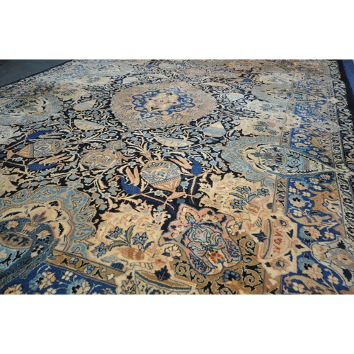 1300 - A LARGE WOOLLEN CREAM GROUND RUG, with a repeating foliate pattern, within a dark blue field, and a ... 